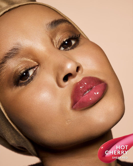 Close-up of a model wearing glossy sheer red lipstick, with a pink product swatch graphic labeled 'HOT CHERRY SHEER RED' in the bottom right corner.
