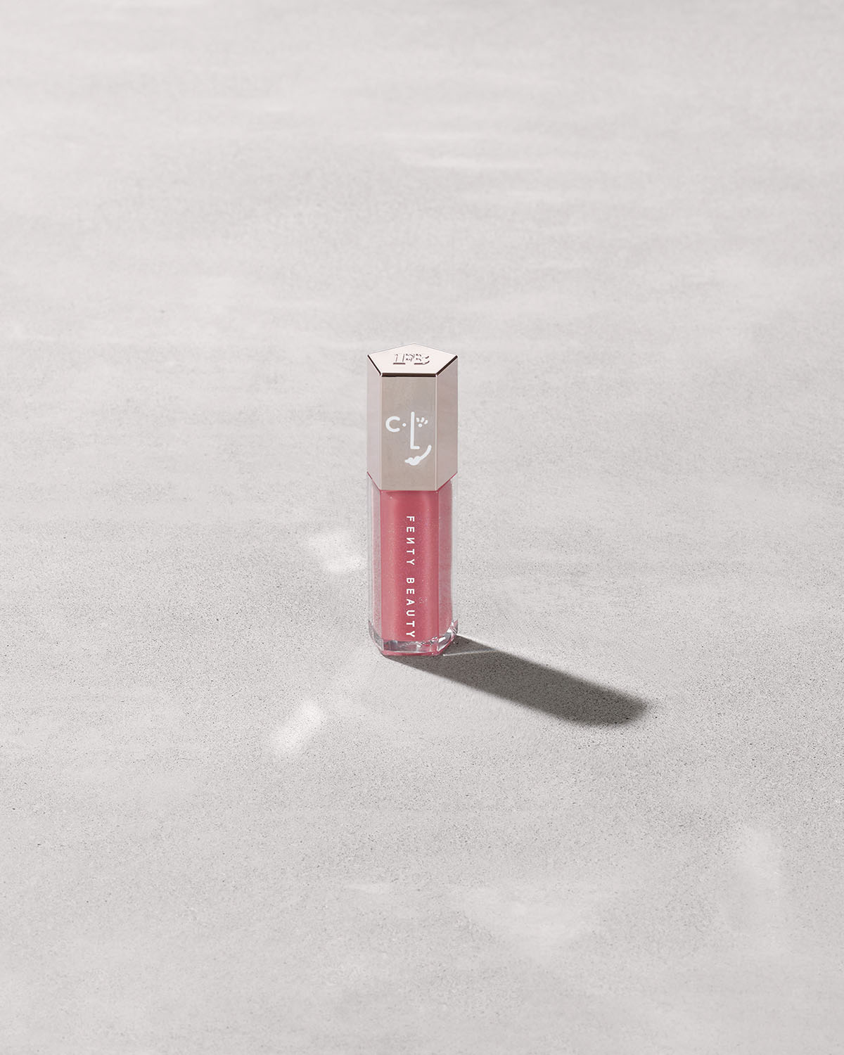 A closed tube of Gloss Bomb Universal Lip Luminizer in the shade Candy Soda on a grey background.
