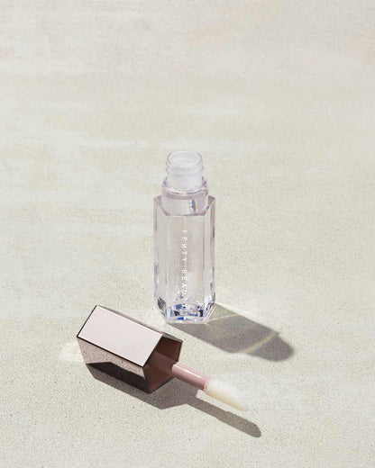 An open tube of Gloss Bomb Universal Lip Luminizer in the shade Glass Slipper on a grey background.